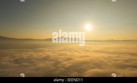 Ein atemberaubender Blick auf den Sonnenaufgang über einem riesigen Wolkenmeer mit fernen Bergsilhouetten unter einem klaren blauen Himmel. Perfekt für Themen der Ruhe, na Stockfoto