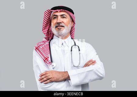 Saudischer Oberarzt in traditionellem Do und Gghutra mit Stethoskop, Arme überkreuzt und wegblickend, selbstbewusster und erfahrener Mediziner ag Stockfoto