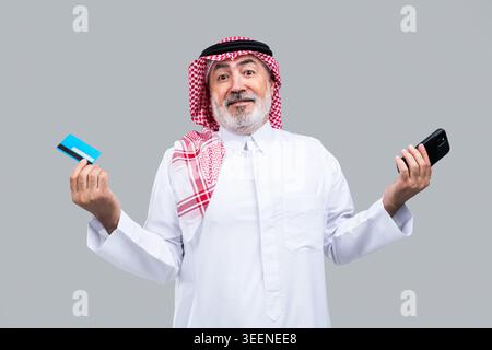 Saudischer Seniorenmann mit Kreditkarte und Smartphone, der moderne digitale Zahlungsmethoden und E-Commerce-Komfort für die ältere Generation präsentiert Stockfoto