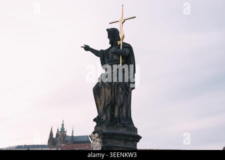 Die Statue des Heiligen Johannes des täufers steht auf der karlsbrücke mit der prager Burg im Hintergrund Stockfoto