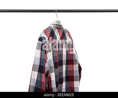 Das karierte Hemd hängt auf einem Metallgestell vor weißem Hintergrund. Das karierte Kleidungsstück liegt auf dem Aufhänger auf und bildet so ein sauberes Display im Kleiderschrank. Minimalistische Mode im Einzelhandel Stockfoto