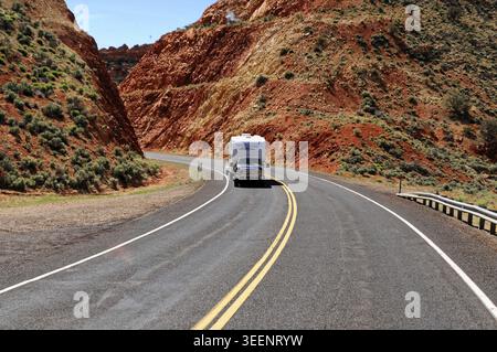 Ein Wohnmobil fährt auf einer kurvenreichen Straße durch eine rote Felsenlandschaft, eine Stahlbrücke in einer trockenen Wüstenlandschaft mit rötlichen Felsen und bogenförmigem Design, Bry Stockfoto