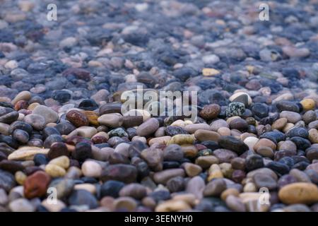 Nahaufnahme von glatten bunten Kieselsteinen unter klarem Wasser, natürlicher Texturhintergrund mit weichem Fokus und ruhiger Seenoberfläche für eine ruhige Stimmung. Stockfoto