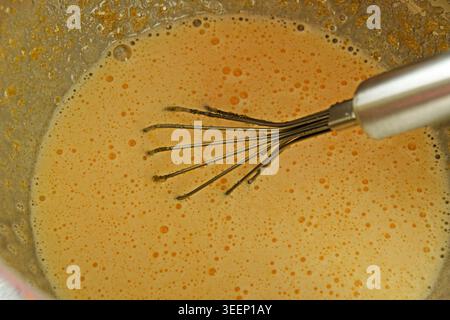 Nahaufnahme eines frisch verquirlten Biskuitteigs in einer Haushaltsmischschschüssel während der Zubereitung von hausgemachten Kuchen in einer echten Wohnküche Stockfoto