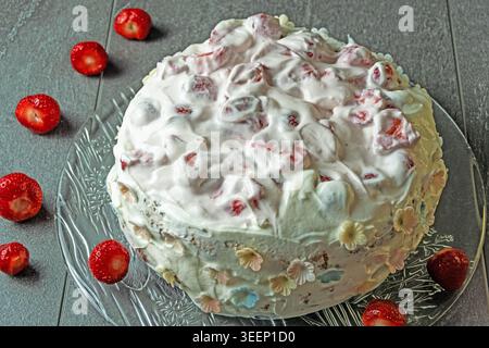 Rustikaler hausgemachter Erdbeercremekuchen mit Schlagsahne-Zuckerguss, frischer Erdbeerfüllung und zusätzlichen Erdbeeren, präsentiert in einem echten Heimkitc Stockfoto