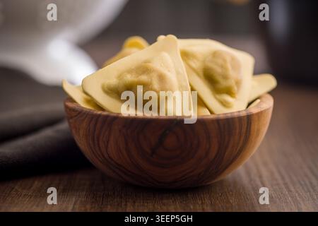 Frische dreieckige Ravioli in einer Holzschale, ungekocht und handgemacht mit sichtbarer Füllung. Nahaufnahme von Speisen, die hausgemachten Komfort und Tradition vermitteln Stockfoto