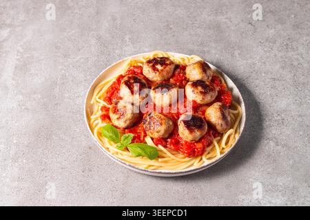 Ein Teller mit klassischen Spaghetti, garniert mit gebräunten Fleischbällchen und reichhaltiger Tomatensauce auf einem leichten Keramikgericht. Stockfoto