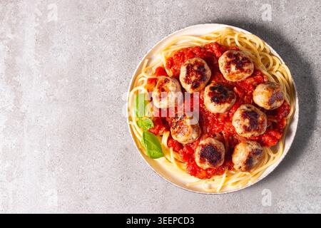 Ein Teller mit klassischen Spaghetti, garniert mit gebräunten Fleischbällchen und reichhaltiger Tomatensauce auf einem leichten Keramikgericht. Stockfoto