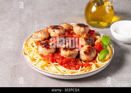 Ein Teller mit klassischen Spaghetti, garniert mit gebräunten Fleischbällchen und reichhaltiger Tomatensauce auf einem leichten Keramikgericht. Stockfoto