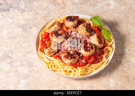 Ein Teller mit klassischen Spaghetti, garniert mit gebräunten Fleischbällchen und reichhaltiger Tomatensauce auf einem leichten Keramikgericht. Stockfoto