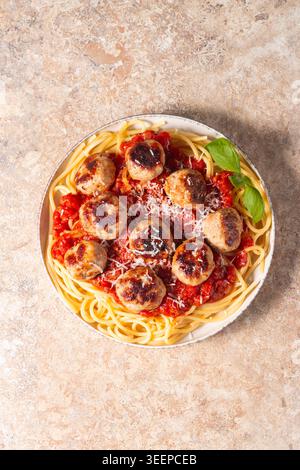 Ein Teller mit klassischen Spaghetti, garniert mit gebräunten Fleischbällchen und reichhaltiger Tomatensauce auf einem leichten Keramikgericht. Stockfoto