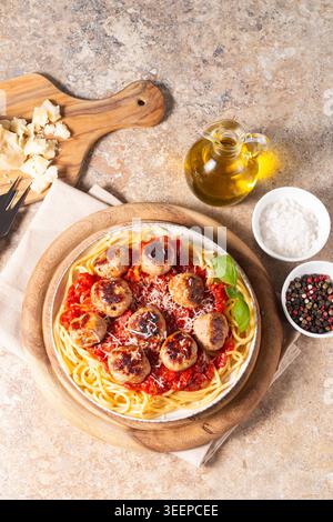 Ein Teller mit klassischen Spaghetti, garniert mit gebräunten Fleischbällchen und reichhaltiger Tomatensauce auf einem leichten Keramikgericht. Stockfoto