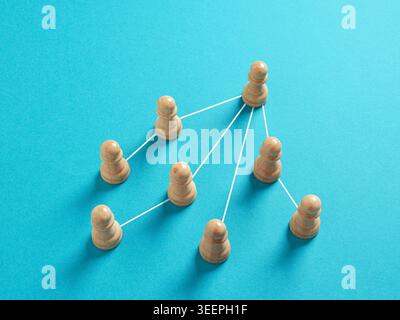Hölzerne Schachfiguren auf blauem Hintergrund, die mit Linien verbunden sind und Hierarchie, Führung, Teamarbeit und Netzwerkstruktur darstellen Stockfoto