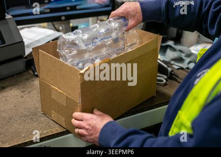 Lagerarbeiter, der Kunststoffpolsterfolie in einen Pappkarton auf einer E-Commerce-Packbank in einem modernen Distributionslager einlegt Stockfoto