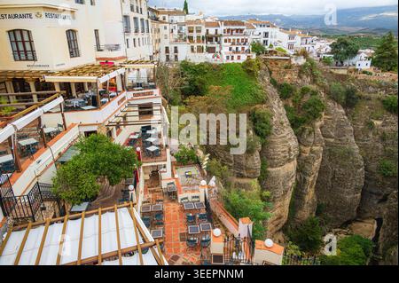 Mehrstöckige Restauranterrassen mit Sitzplätzen im Freien säumen weiße Gebäude am Rande einer steilen Schlucht in Ronda, Andalusien, Spanien. Gesteinsformat Stockfoto