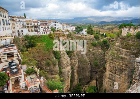 Weiße Gebäude der Stadt Ronda an den Klippen in Andalusien, Spanien, stehen am Rande einer tiefen felsigen Schlucht. Grüne Vegetation, bewirtschaftete Felder, A Stockfoto