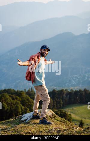 Ein lächelnder Mann steht auf einem Bergrücken mit weit offenen Armen und überblickt das Tal bei Raghupur Fort, Sojha, Manali, Himachal Pradesh, Indien. Stockfoto