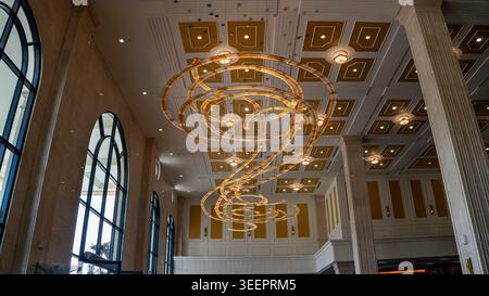 Große Lobby-Innenausstattung mit spektakulären spiralförmigen goldenen Kronleuchtern, die an einer kunstvoll verzierten Decke aus Gold und weiß hängen. Hohe Bogenfenster Stockfoto