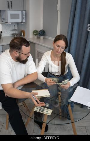 Ein Paar, das an einem Tisch in der Küche sitzt, Geld zählt und Berechnungen in einem Notizbuch macht, Familienkosten verwaltet und den Haushalt plant Stockfoto