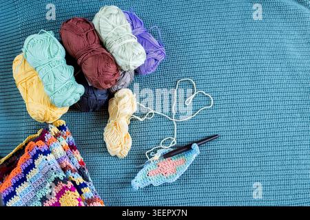Bunter Häkelarbeitsbereich mit Garn-Knäueln und handgefertigtem Granny Square auf blauem gestricktem Hintergrund Stockfoto