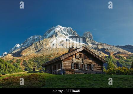 Auberge La Boerne, Frankreich - 18.09.2025: Hölzernes Chalet auf einer grünen Wiese mit schneebedeckten Bergen und Nadelwäldern unter klarem blauem Himmel. Stockfoto
