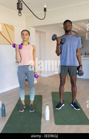 Afroamerikanisches Paar, das zu Hause Bizepslocken auf grünen Matten macht und lila, schwarze Kurzhanteln hält Stockfoto