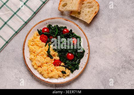 Gekochtes Omelette und Spinat mit Tomaten auf hellem Hintergrund, Blick von oben. Stockfoto