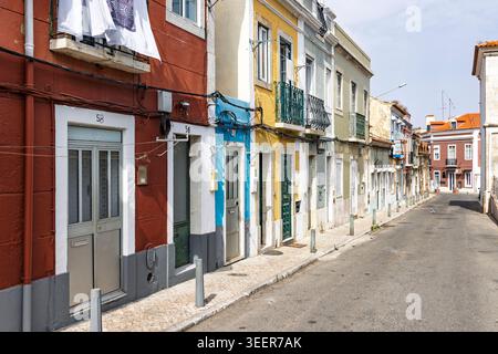 Setubal, Portugal, 16. August 2025. Enge Straße mit leuchtenden roten, blauen und gelben Häusern, deren Kleidung auf den Balkonen der historischen Altstadt trocknet Stockfoto
