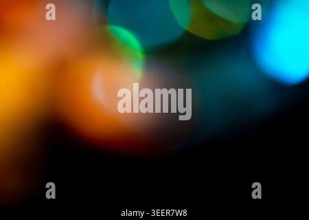 Bokeh-Lichter verschwimmen mit leuchtenden gelben, orangen, grünen und blauen Farben vor dunklem Hintergrund und bilden ein schönes, weiches abstraktes Muster, ideal für Stockfoto