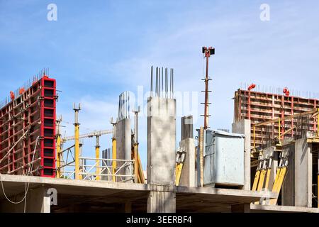 Mehrstöckiges Betongebäude im Bau vor klarem blauem Himmel. Er verfügt über eine markante rote Schalung, tragende Säulen und verstärktes Gestell Stockfoto