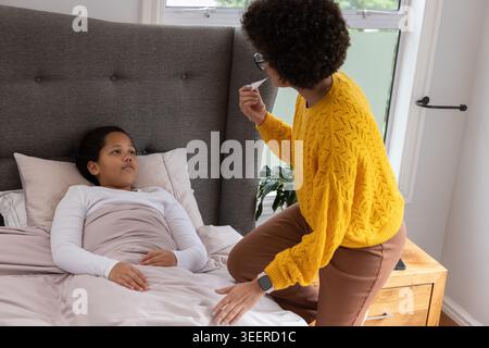 Afroamerikanische Mutter und Kind kniend, Mutter mit Thermometer im Schlafzimmer Stockfoto