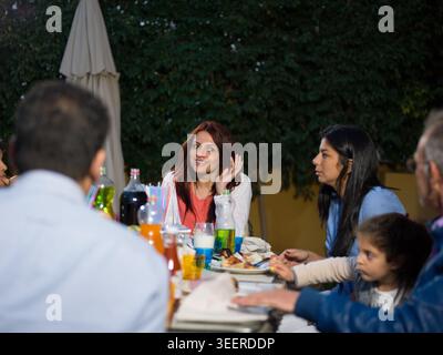 Familien aus dem Nahen Osten, die mehrere Generationen lang in einer modernen Luxusvilla mit Freunden und Kindern ein Abendessen im Freien genießen Stockfoto