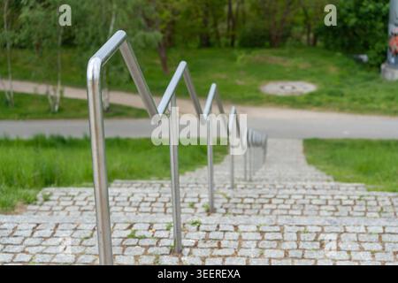 Der Handlauf aus Metall führt über Steinstufen. Grüner Gras und Bäume umgeben den Pfad im Park. Unscharfer Hintergrund erzeugt Tiefe. Perfekt für urbanes Design Stockfoto