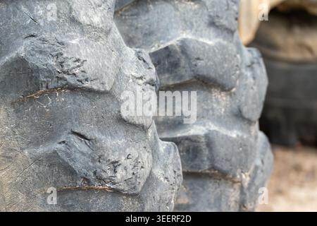 Nahaufnahme des Profils schwerer Traktorreifen, bedeckt mit Staub und Schmutz. Tiefe Rillen zeigen Verschleiß aus rauem Gelände. Ideal für Landwirtschaft, Bauwesen oder i Stockfoto
