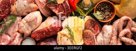 Verschiedene Fleischstücke sind auf dunkler Oberfläche angeordnet. Rindersteaks, Wachteln, Schweinefleischwürste, truthahn, Huhn, und Schweinefleisch sind zusammen mit Kräutern und spi vorhanden Stockfoto