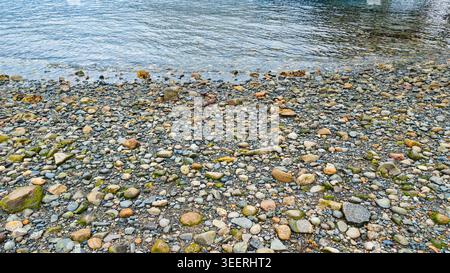 Kieselstrand. Wellen krachen sanft auf bunten kleinen Felsen. Aufnahme in sanfter natürlicher Beleuchtung, neutrale Töne und verschiedene Texturen geeignet Stockfoto
