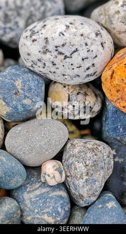 Verschiedene Flusssteine stapeln sich und zeigen Texturen. Weiches, gerichtetes Licht betont die glatten Oberflächen und natürlichen Farbvariationen. Könnte gut für gut sein Stockfoto
