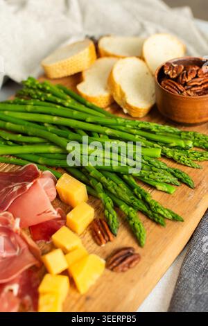 Verwöhnen Sie sich mit einer wunderschön gestalteten Wurstplatte mit lebhaftem Spargel, herzhaftem Wurstwaren, verschiedenen Käsesorten und frisch geröstetem Brot, ideal für Stockfoto