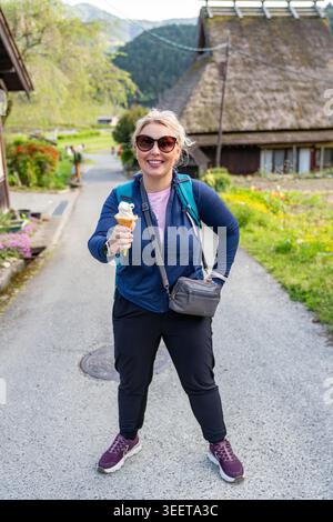 Die blonde Touristenfrau hält eine Eiskugel, während sie das traditionelle japanische Dorf Miyama erkundet Stockfoto