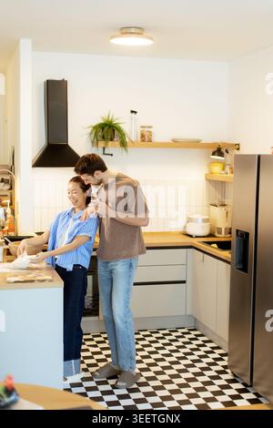 In einer modernen Küche kochen eine Koreanerin und ein Kaukasier zusammen. Sie teilen ein Lächeln, während sie Essen zubereiten. Die Küche hat ein stilvolles Design Stockfoto