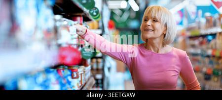 Frau, die tagsüber im Lebensmittelgeschäft einkaufen möchte, wählt Artikel aus dem Regal Stockfoto