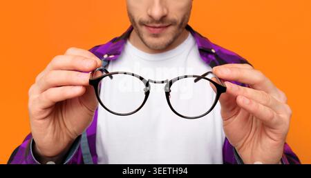 Der Mann hält eine runde Brille vor orangefarbenem Hintergrund, während er nachdenklich aussieht Stockfoto