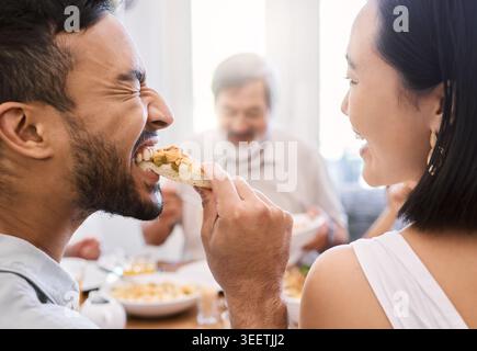 Familie, Paar und Essen zu Hause mit lustigem Witz, verspieltem Biss und Verbundenheit am Wochenende. Glückliche, verheiratete Leute und Humor im Speisesaal Stockfoto