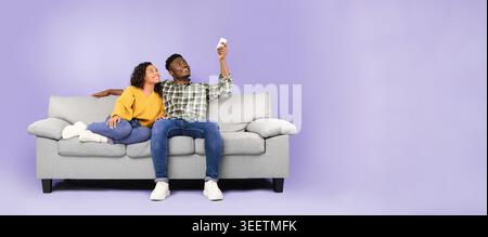 Ein Paar genießt die Zeit zusammen auf einem Sofa, während es ein Selfie in einem Purple Room macht Stockfoto