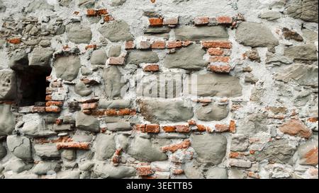 Alte Stein- und Ziegelmauerstruktur mit einer veralteten Oberfläche, die natürliche Abnutzung und organische Mängel zeigt. Stockfoto