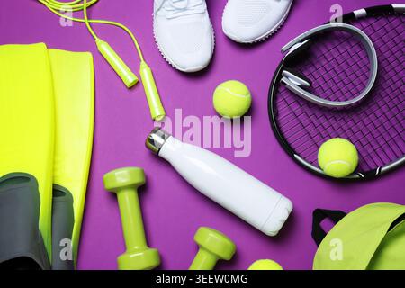 Sportausrüstung, Turnschuhe, Kopfhörer und Wasserflasche auf violettem Hintergrund, flach gelegen Stockfoto