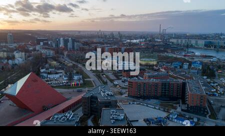 Blick auf den Sonnenuntergang von Danzig, Polen, mit rotem Dach, Apartmentkomplexen, Industriehafen mit Kränen und Uferpromenade Stockfoto