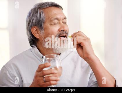Alter Mann, Pillen und Wasser mit Wellness zu Hause für Nahrungsergänzungsmittel, Medizin und Omega 3. Asiatische Person, Glas und Kapsel für Vorteile, Pharma Stockfoto