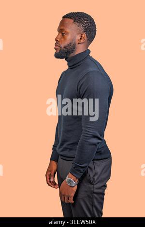 Mann in schwarzem Rollkragenpullover und schwarzer Hose in Profilansicht vor schlichtem Hintergrund Stockfoto