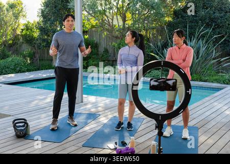 Fitnesstrainer mit zwei Auszubildenden, die an Deck am Pool mit Ringlicht trainieren Stockfoto